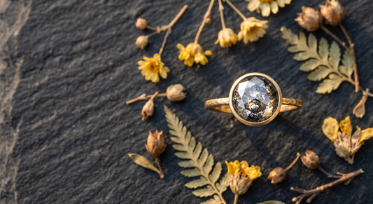 Salt and pepper diamond engagement ring in yellow gold bezel setting on dark slate with dried wildflowers for the complete buying guide